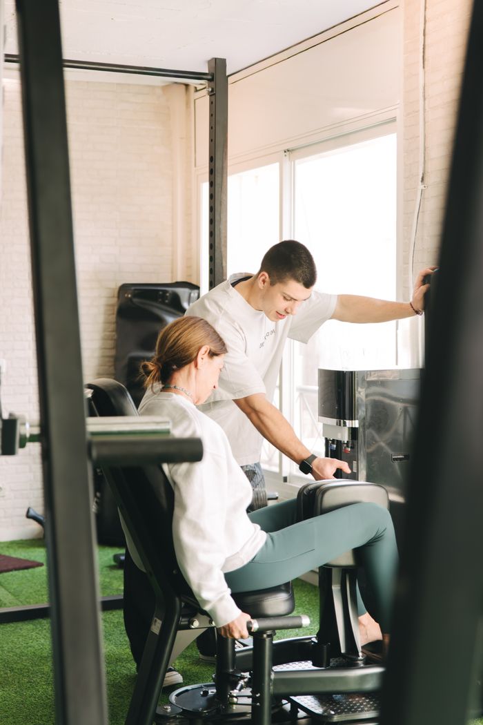 Entrenador personal guiando a una clienta en una máquina de gimnasio