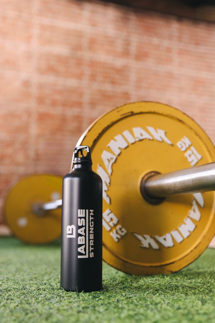 Botella y disco de pesas amarillo sobre césped de gimnasio